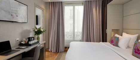A modern hotel room with a bed, desk, and computer.