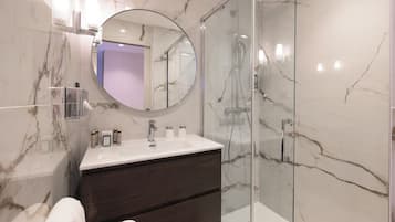 A modern bathroom with a marble vanity, a round mirror, and a glass-enclosed shower.