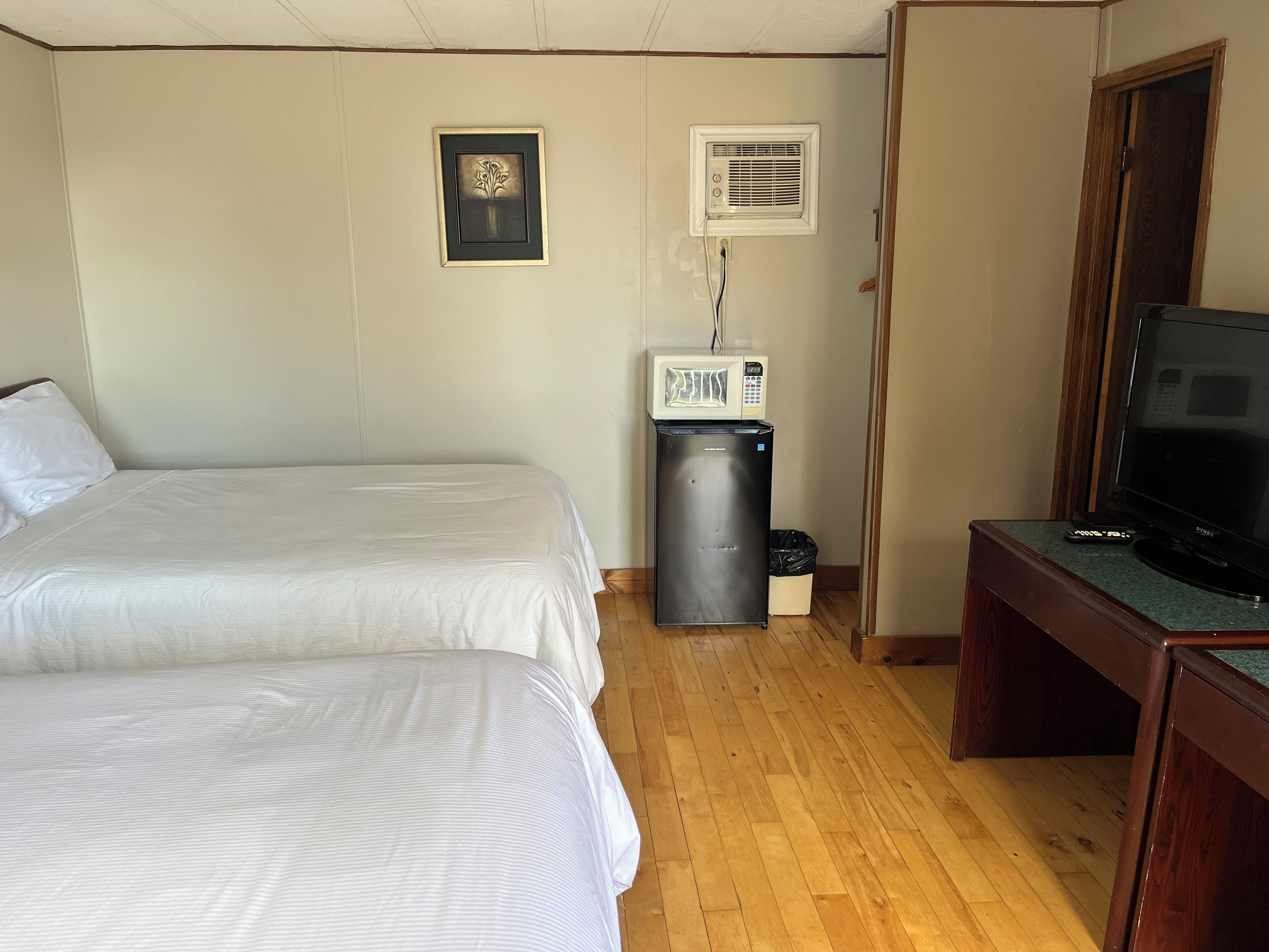 A hotel room with two beds, a microwave, a trash bin, and a television.