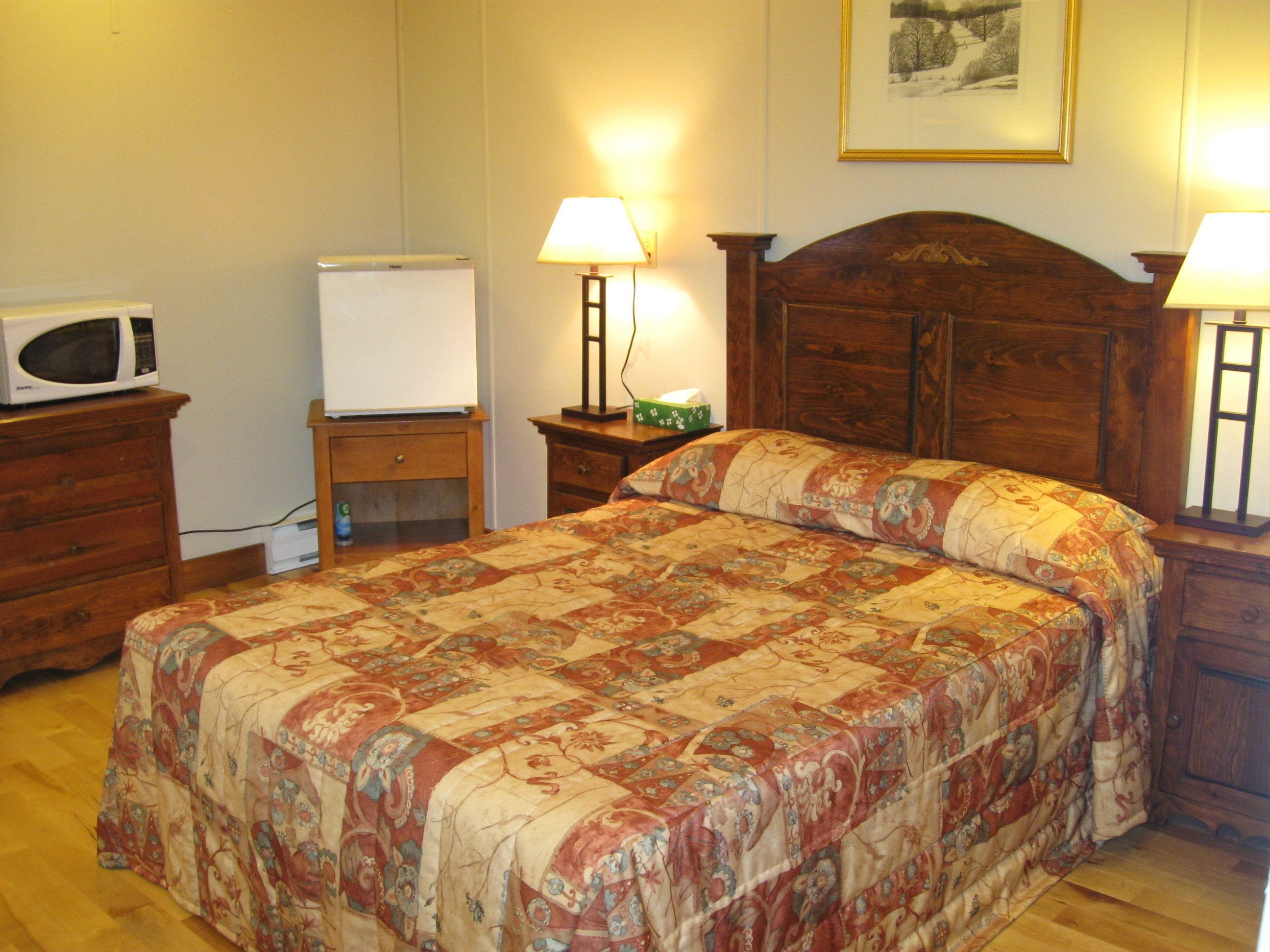 Un dormitorio con una cama de madera, dos mesitas de noche con lámparas, un aparador, un microondas y una pizarra.