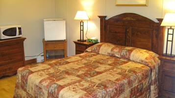 Un dormitorio con una cama de madera, dos mesitas de noche con lámparas, un aparador, un microondas y una pizarra.