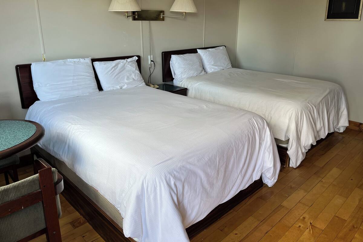 Une chambre d’hôtel avec deux lits simples, une petite table ronde et une chaise.