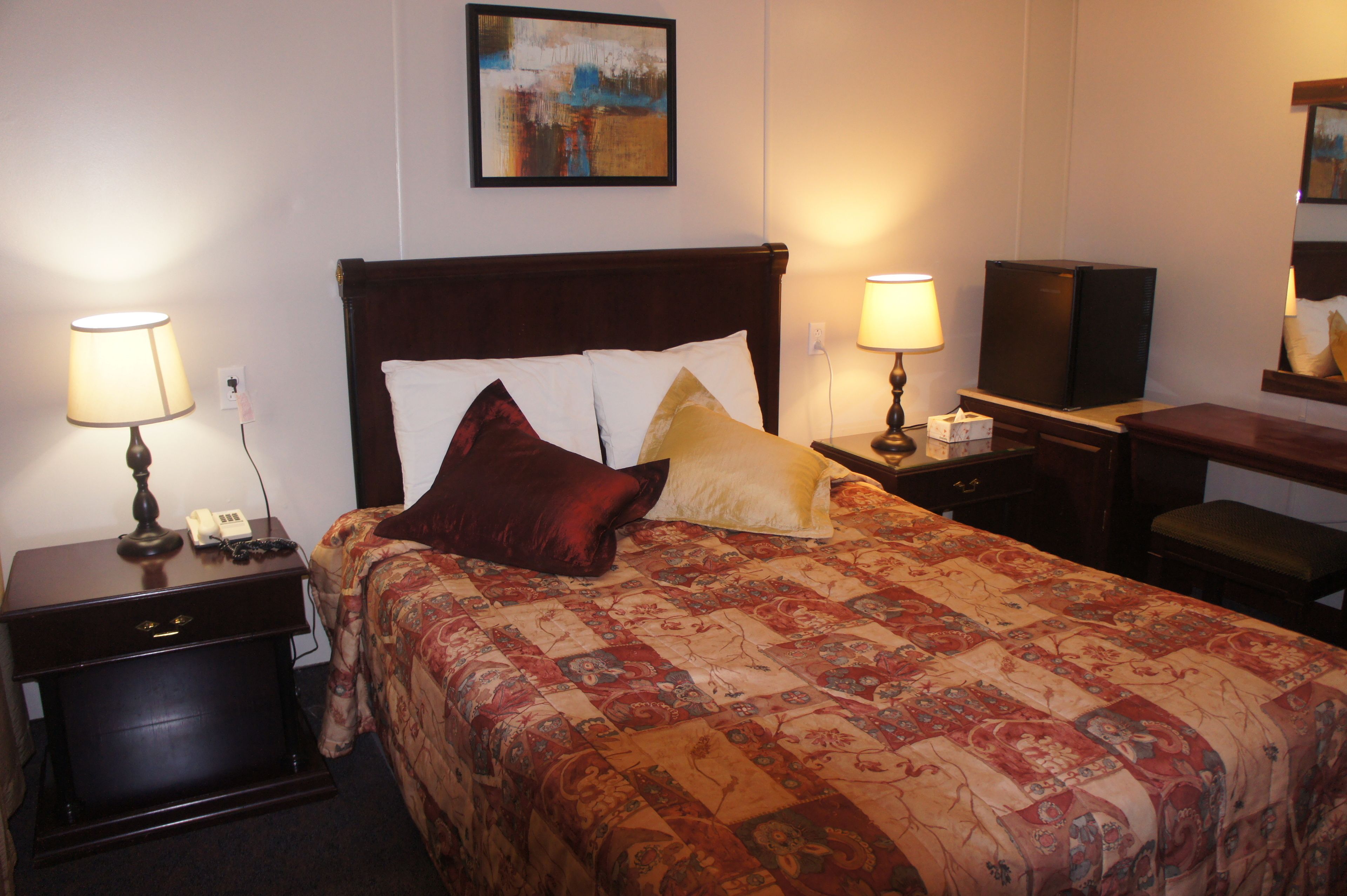 A hotel room with a large bed, two bedside tables with lamps, a desk with a television, and a painting on the wall.