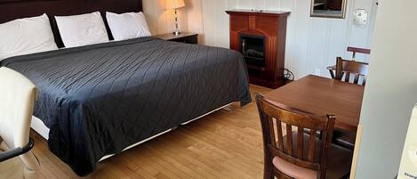 A hotel room with a bed, a desk, a chair, a lamp, and a fireplace.
