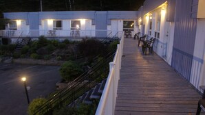 Una terraza de madera con mobiliario exterior y vistas a un edificio con varias ventanas y puertas.