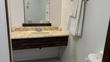 Une salle de bain avec des toilettes blanches, un lavabo doté d’un plan de travail en marbre, un miroir et un porte-serviettes.