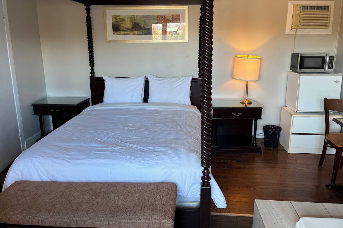 Une chambre d’hôtel avec un lit à baldaquin, une lampe de chevet, un four à micro-ondes, un réfrigérateur et une chaise.