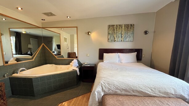 Habitación de hotel con una cama grande, un baño privado con bañera, piso de madera y un espejo amplio.