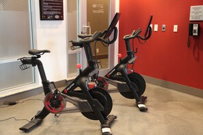 Deux vélos d’appartement dans une pièce dont un mur est rouge et où l’on aperçoit une porte au fond.