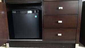 Un mueble de madera oscura con un refrigerador negro integrado, varios cajones y un pequeño logo en el refrigerador.