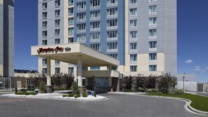 Un hotel Hampton Inn con una fachada moderna, varios pisos y un cielo despejado.