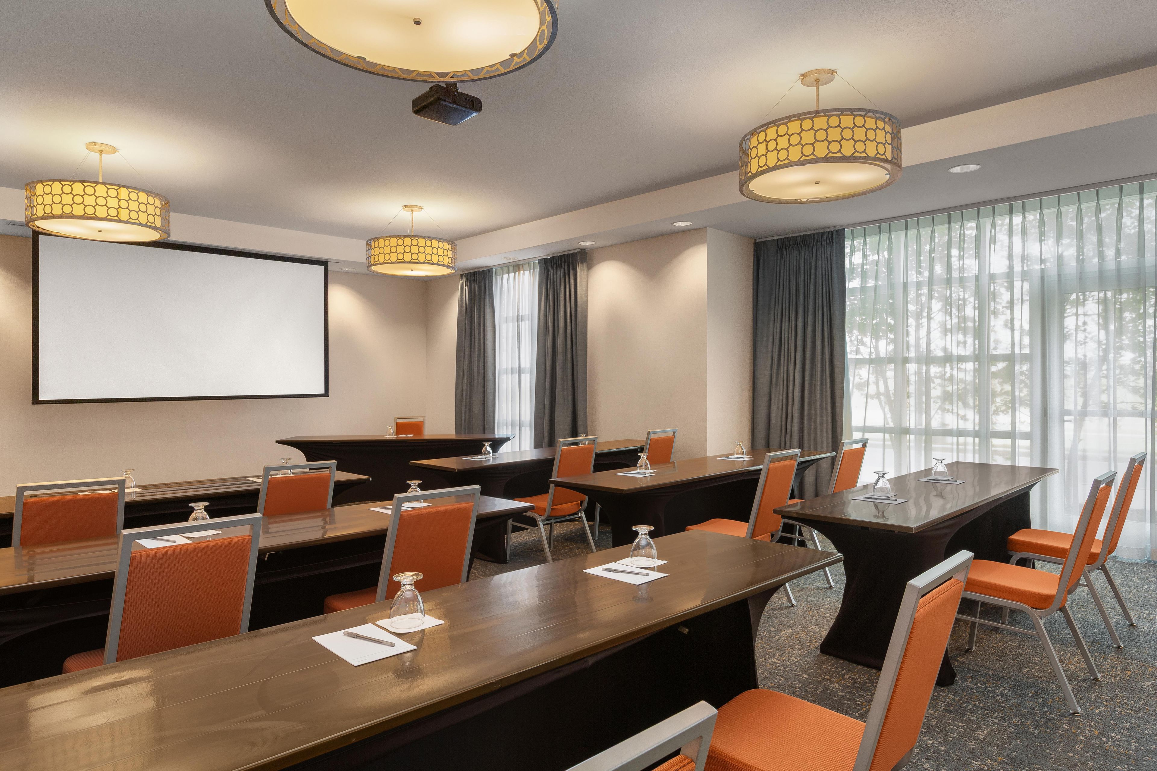 A conference room with a large table, chairs, a projector screen, and pendant lighting.