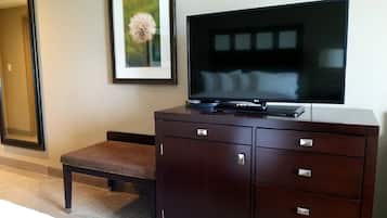 A hotel room with a dark wooden cabinet, a flat-screen TV, a framed picture of a flower, and a bench.