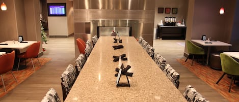A conference room with a long table, chairs, a coffee station, and a TV screen.