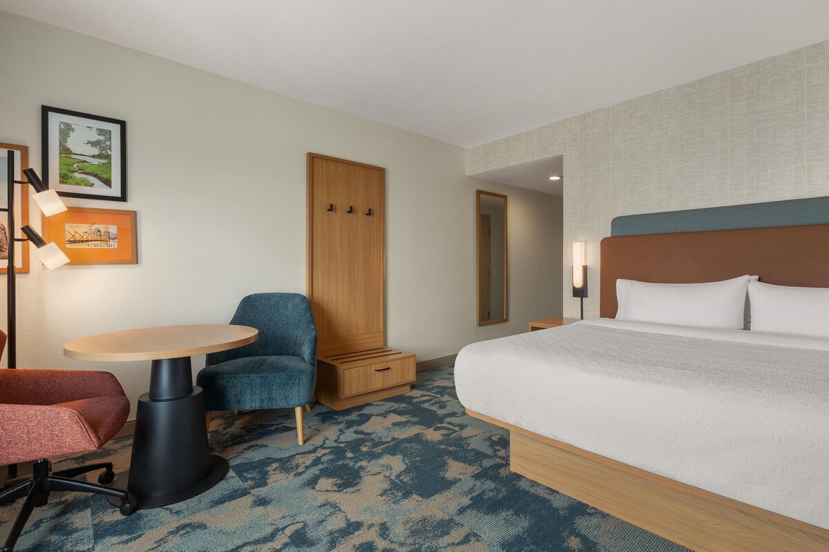 A hotel room with a bed, a desk, a chair, a wardrobe, and a carpeted floor.