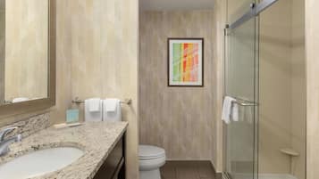 A bathroom with a granite countertop sink, a toilet, and a glass shower enclosure.