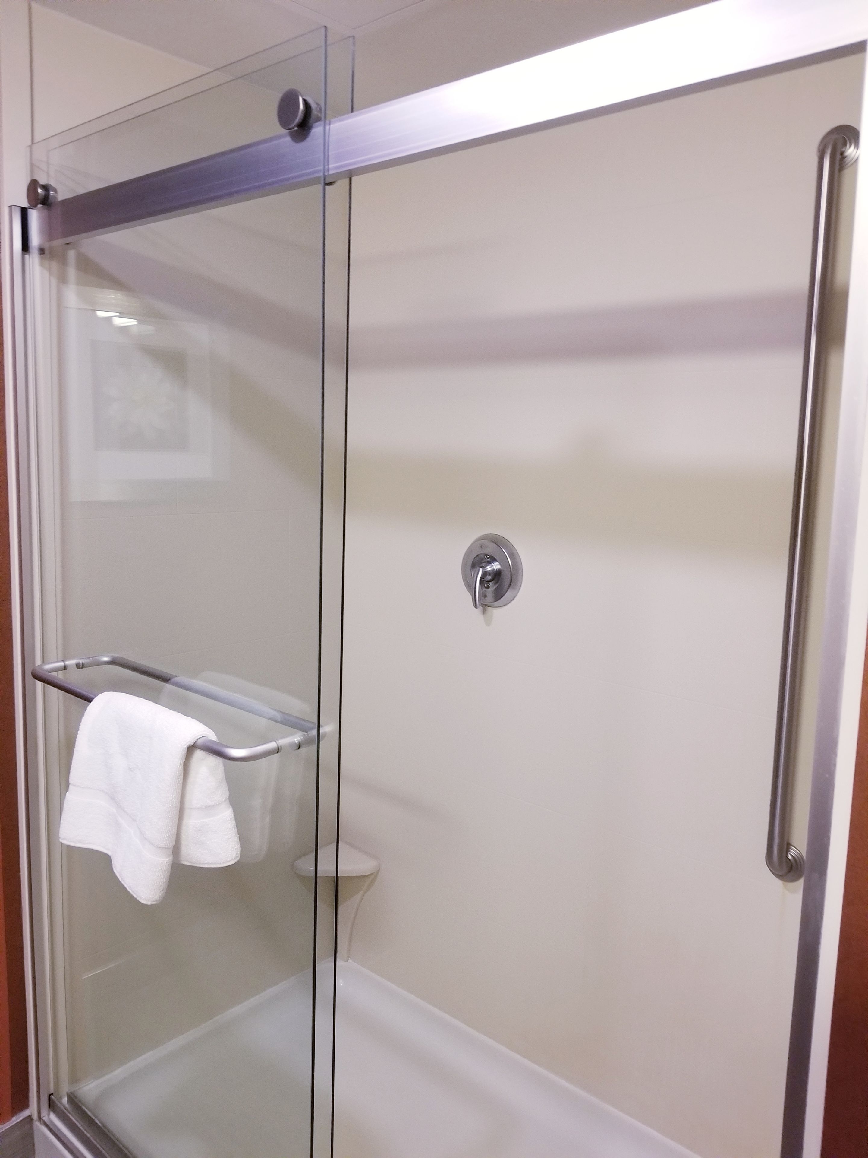 A glass-enclosed shower with a white towel on a metal rack.