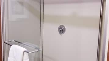 A glass-enclosed shower with a white towel on a metal rack.