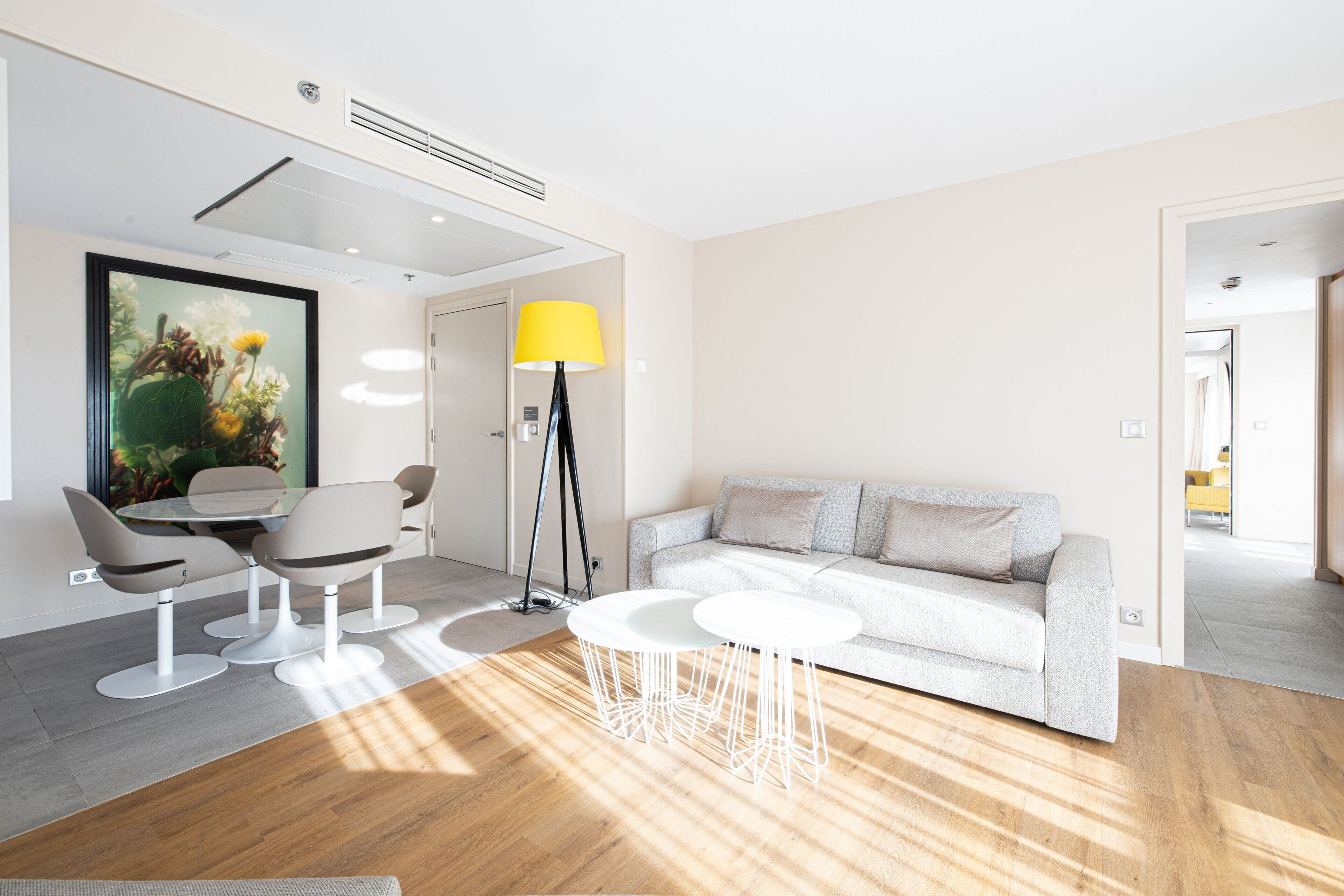 Una sala de estar moderna con un sofá, una mesa de comedor con sillas, una lámpara de pie y un cuadro grande.