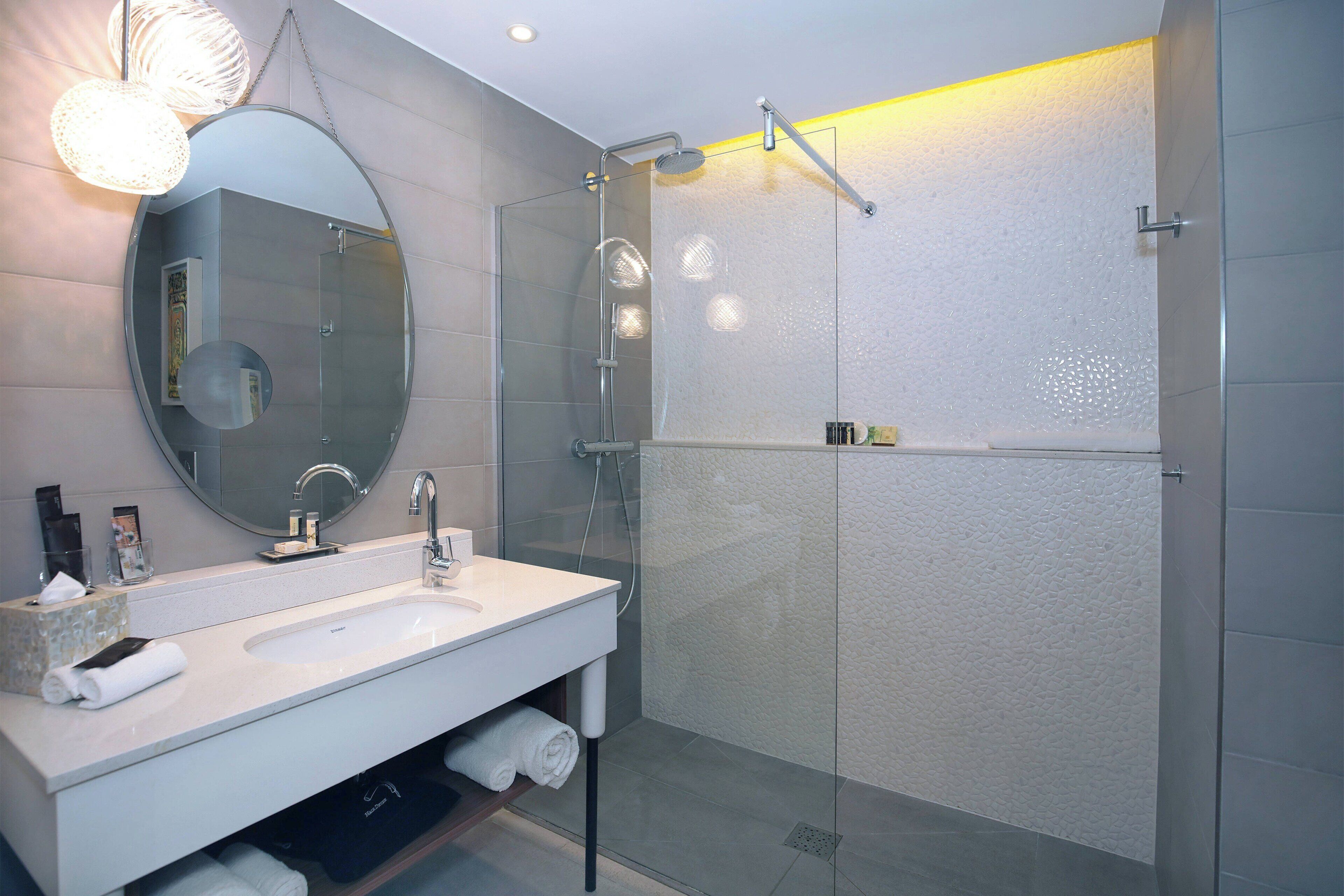 Un baño moderno con ducha de vidrio, un espejo grande y un tocador blanco.
