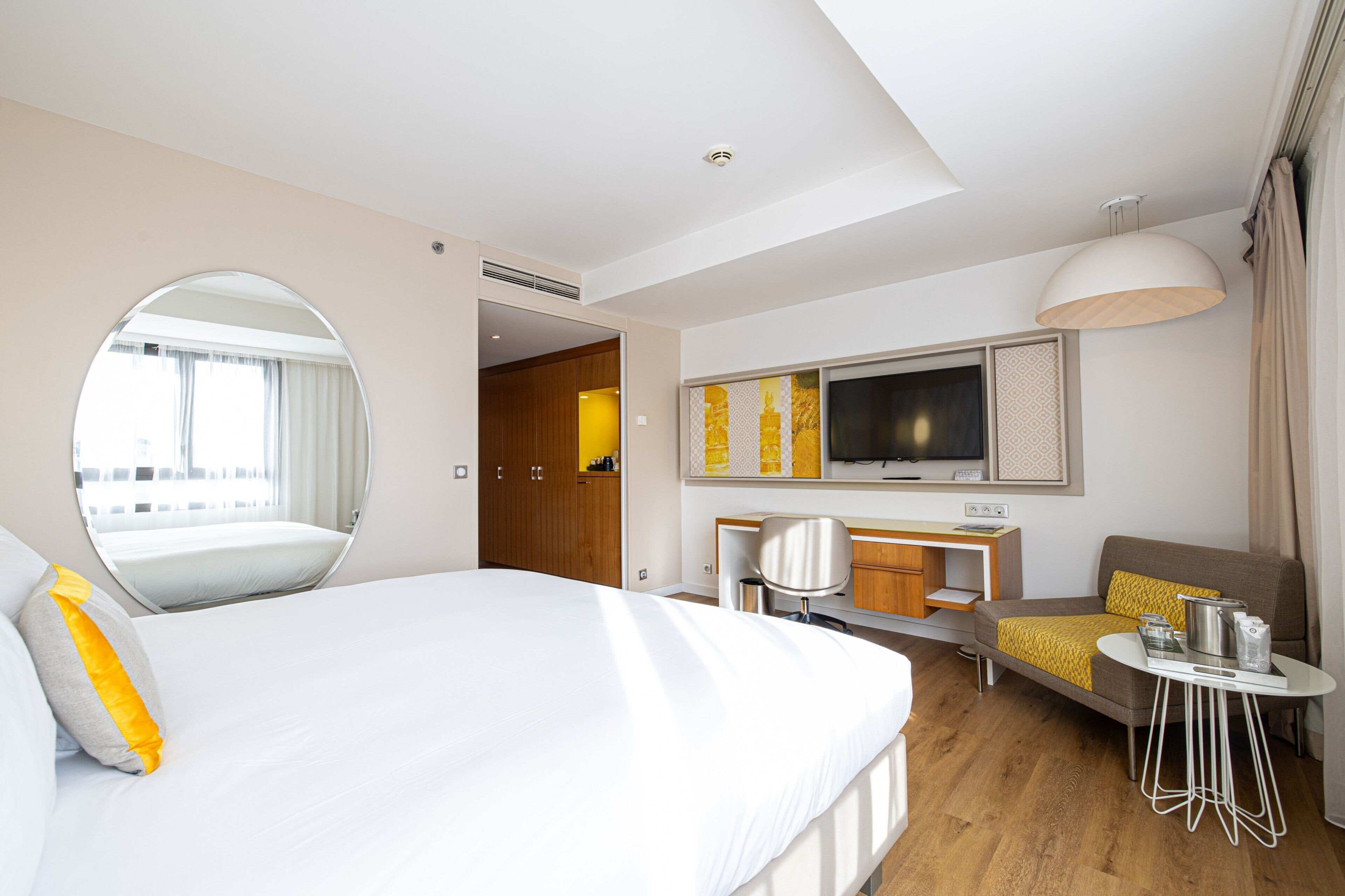 A hotel room with a bed, a desk, a chair, a TV, and a dining area.