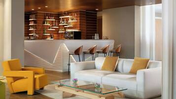 A modern living area with a white sofa, yellow armchair, and glass coffee table. A bar area with shelves of bottles and glasses is visible in the background.
