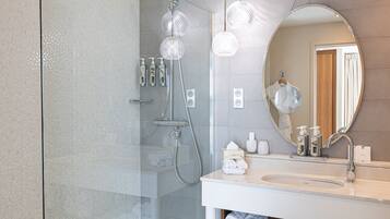A modern bathroom with a glass shower enclosure, a round mirror, and a white sink with toiletries.