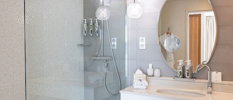 Um banheiro moderno com box de vidro, espelho redondo e pia branca com amenities.