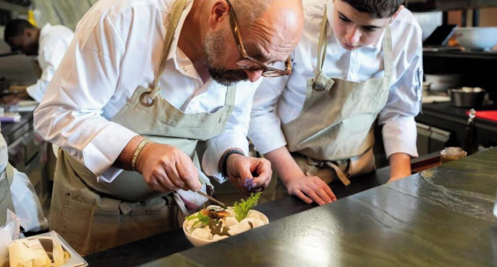 Two individuals in a kitchen setting, one preparing food.