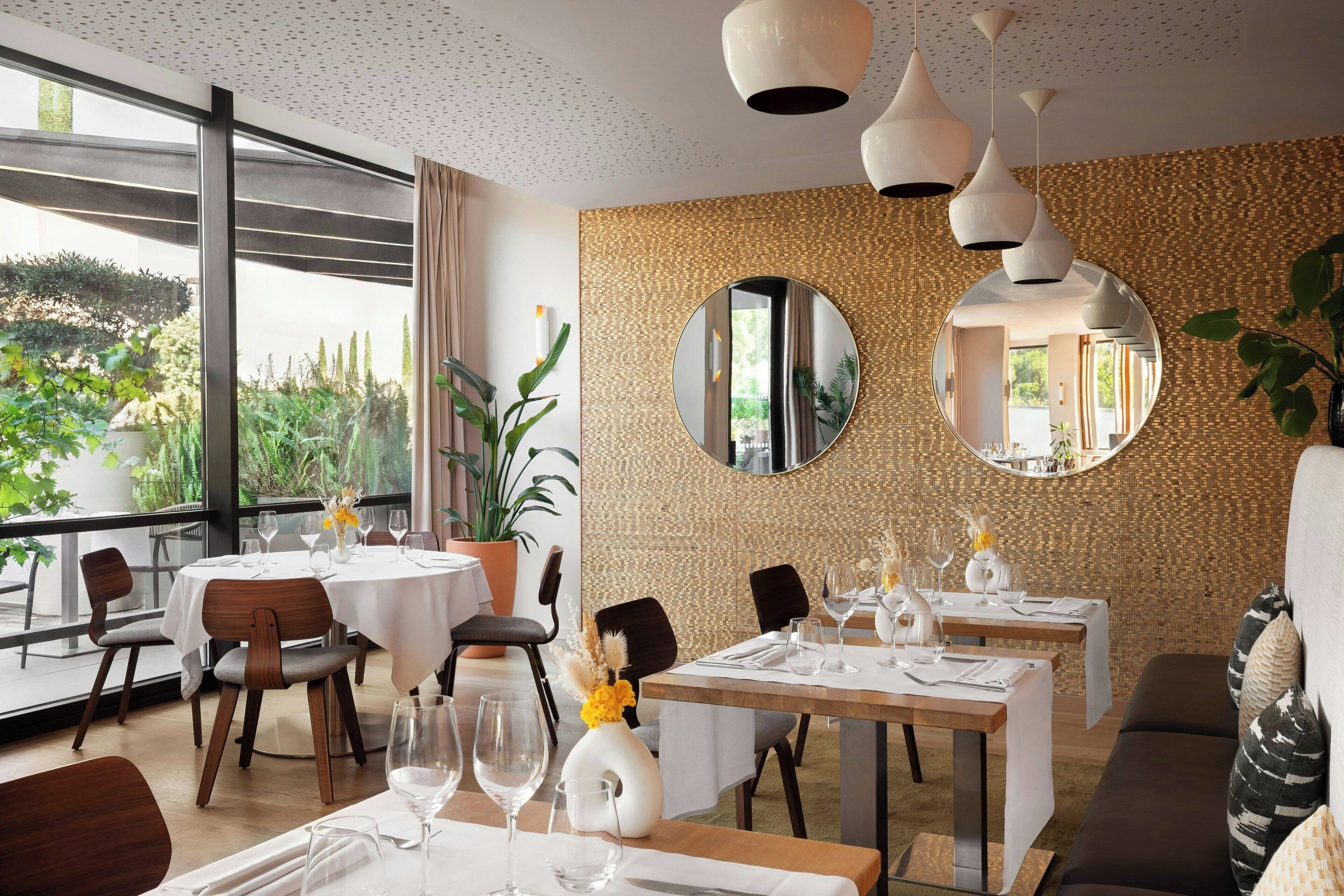 A restaurant with round tables, chairs, and hanging pendant lights.