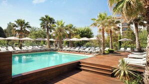 A pool area with lounge chairs and umbrellas, surrounded by palm trees and a building in the background. - Renaissance Aix-en-Provence Hotel (Aix-en-Provence)