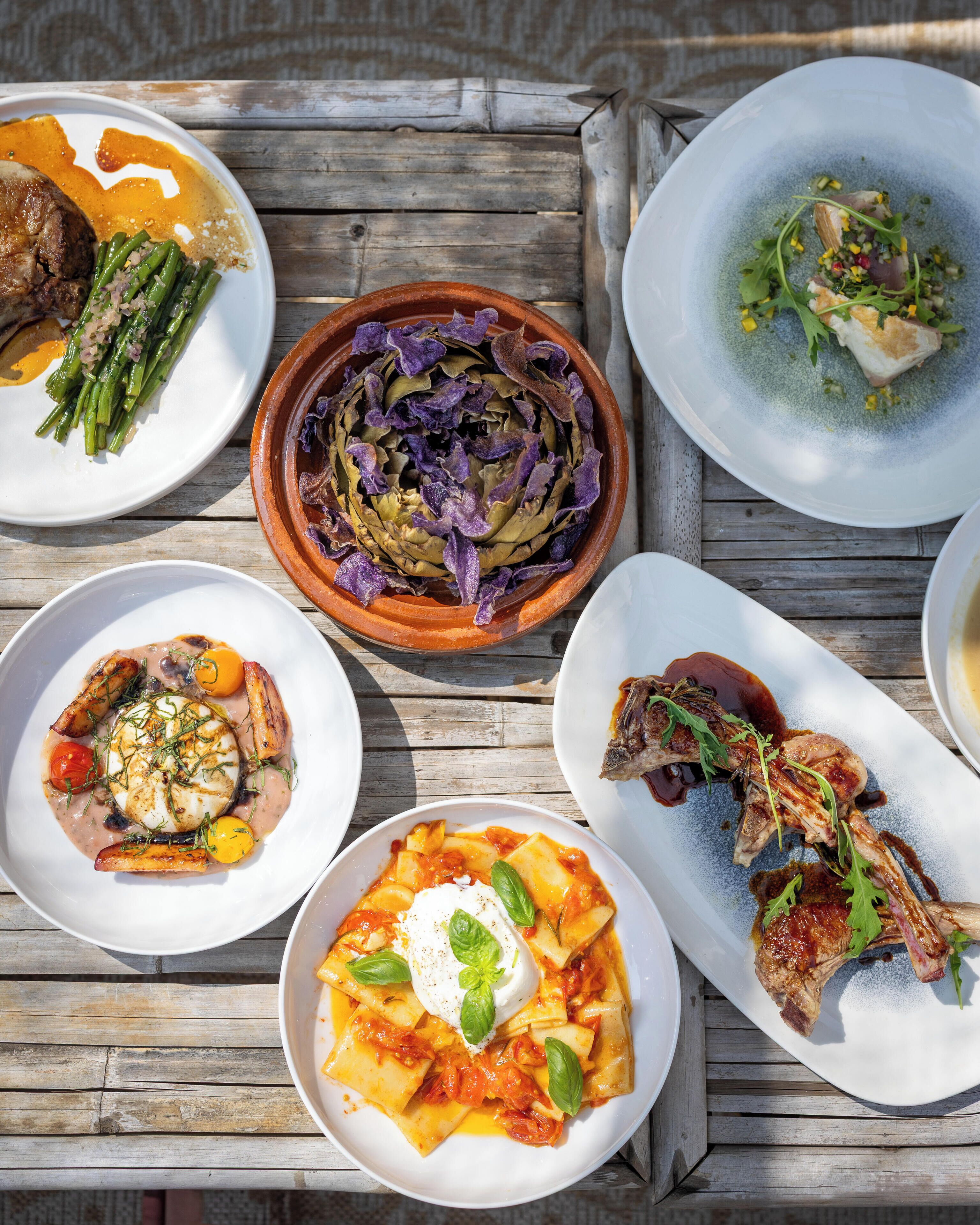 A wooden table with various dishes including pasta, meat, and vegetables.