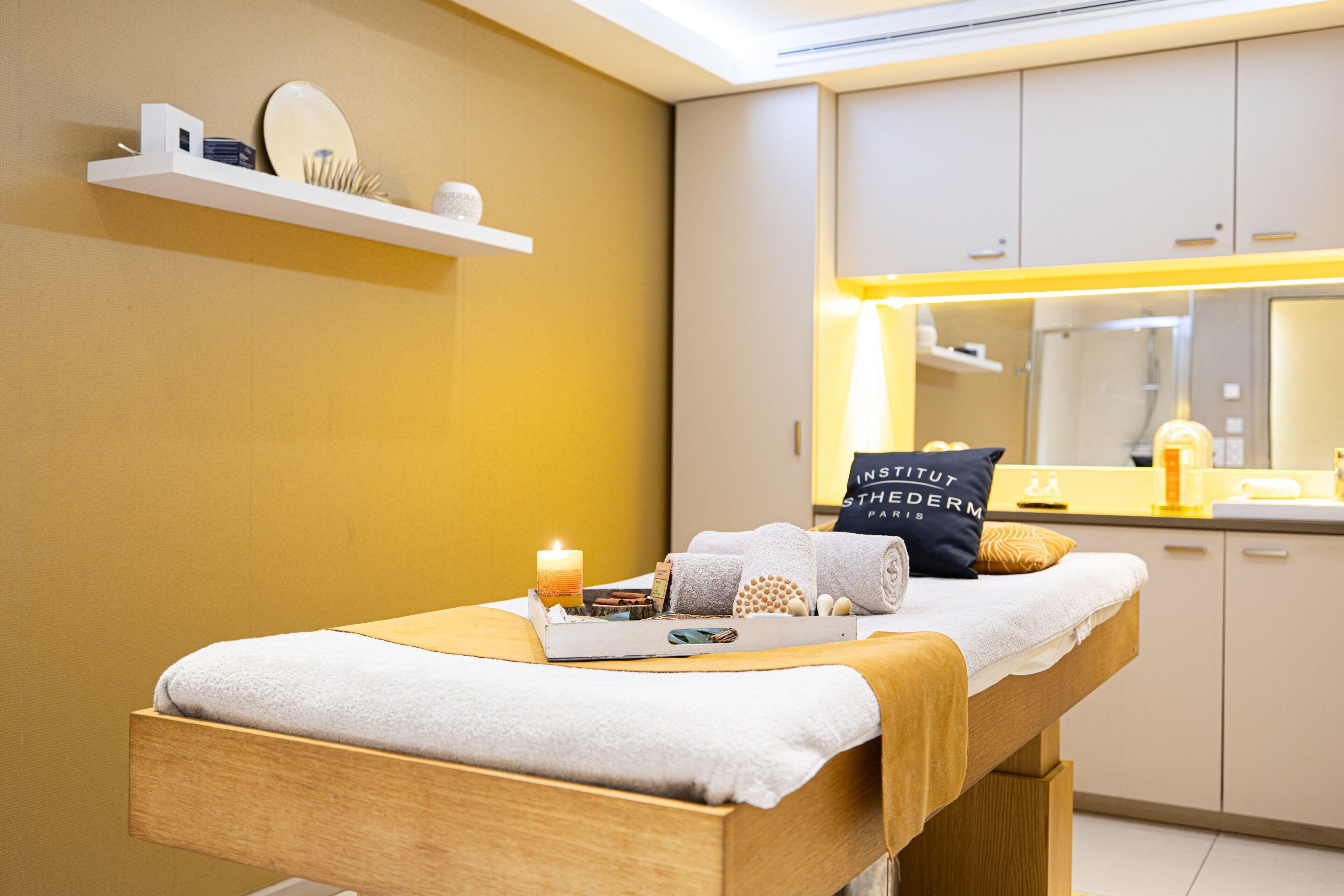 Une salle de soins avec une table de massage en bois, des serviettes, des bougies et une étagère contenant des articles de toilette.