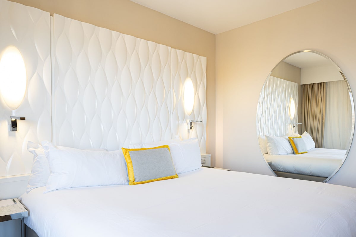 Une chambre d’hôtel avec un grand lit, un miroir rond et une tête de lit à motifs.