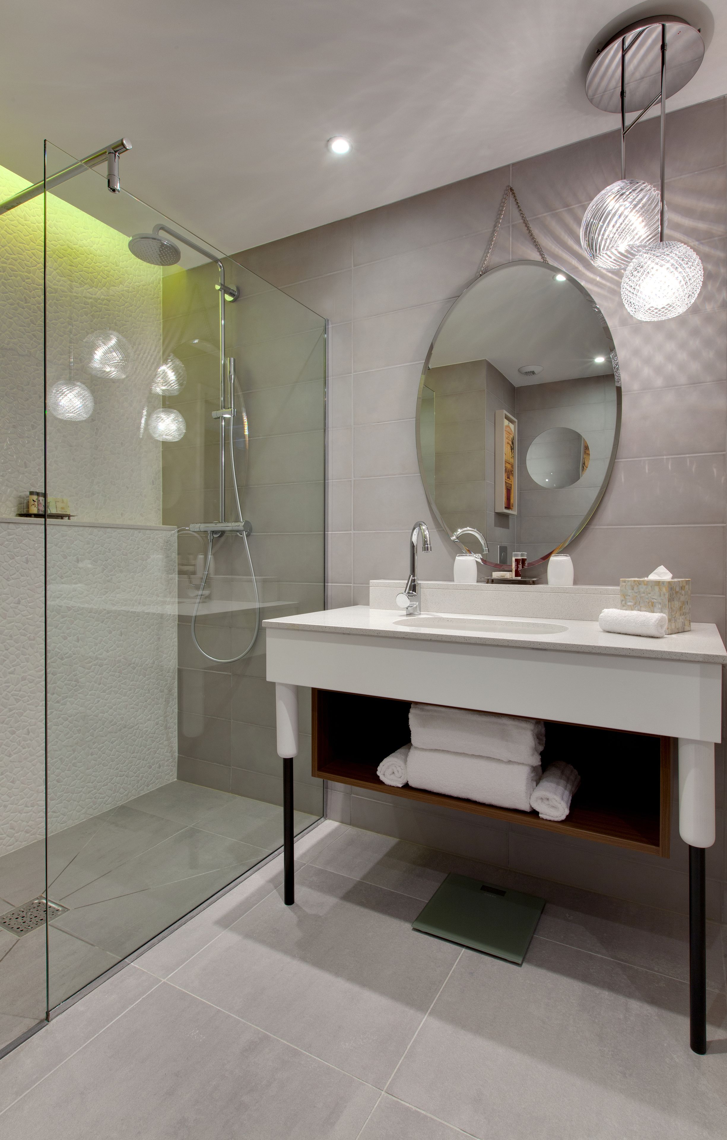 Une salle de bain moderne avec une douche à parois de verre, un lavabo blanc avec un miroir au-dessus et un porte-serviettes avec des serviettes pliées.