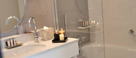 A bathroom with a white sink, a mirror, a glass shower enclosure, and a lit candle on the counter.
