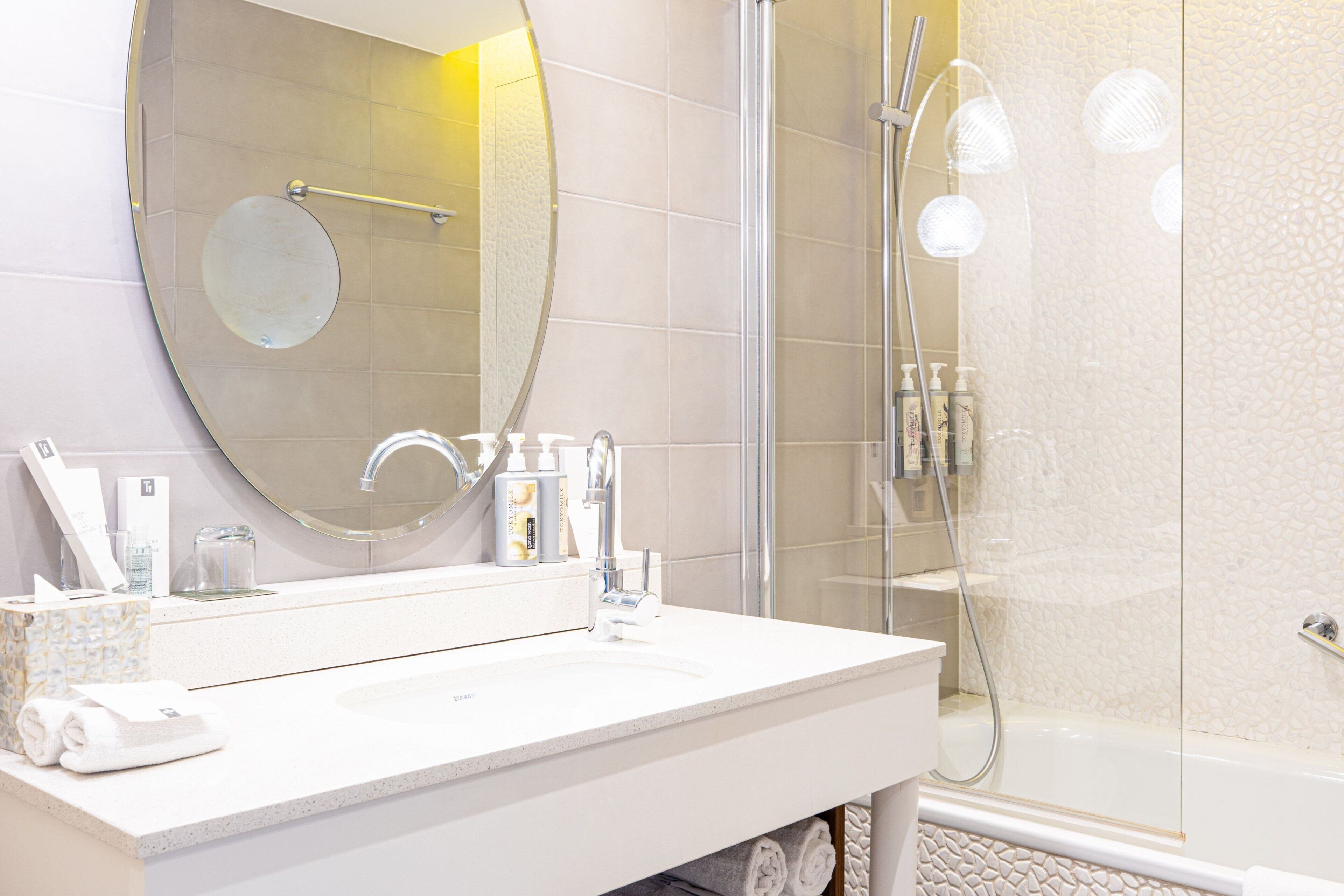 Een moderne badkamer met een ronde spiegel, een witte wastafel en een douche met glazen wanden.