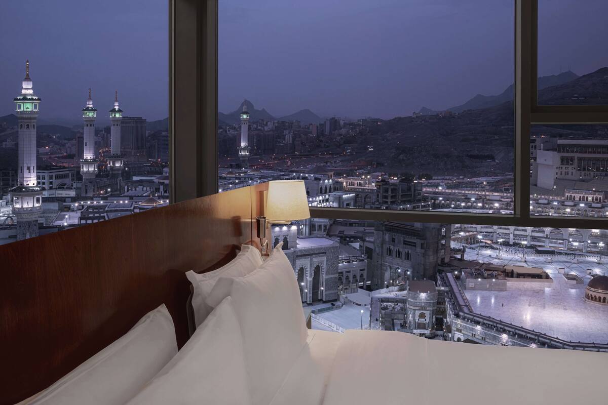 Habitación de hotel con un ventanal grande que da a un paisaje urbano, incluyendo una mezquita con minaretes iluminados.
