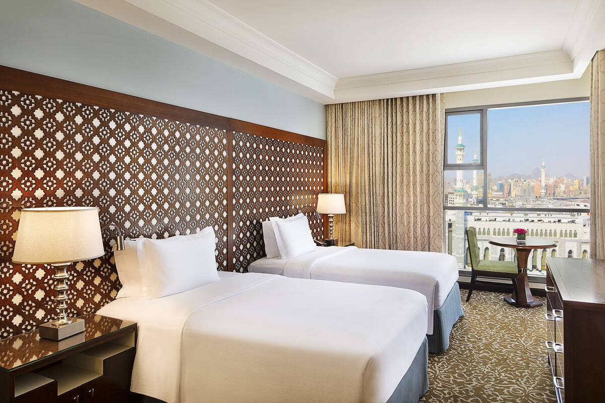 Habitación de hotel con dos camas, vista a la ciudad y un balcón con mesa y silla.