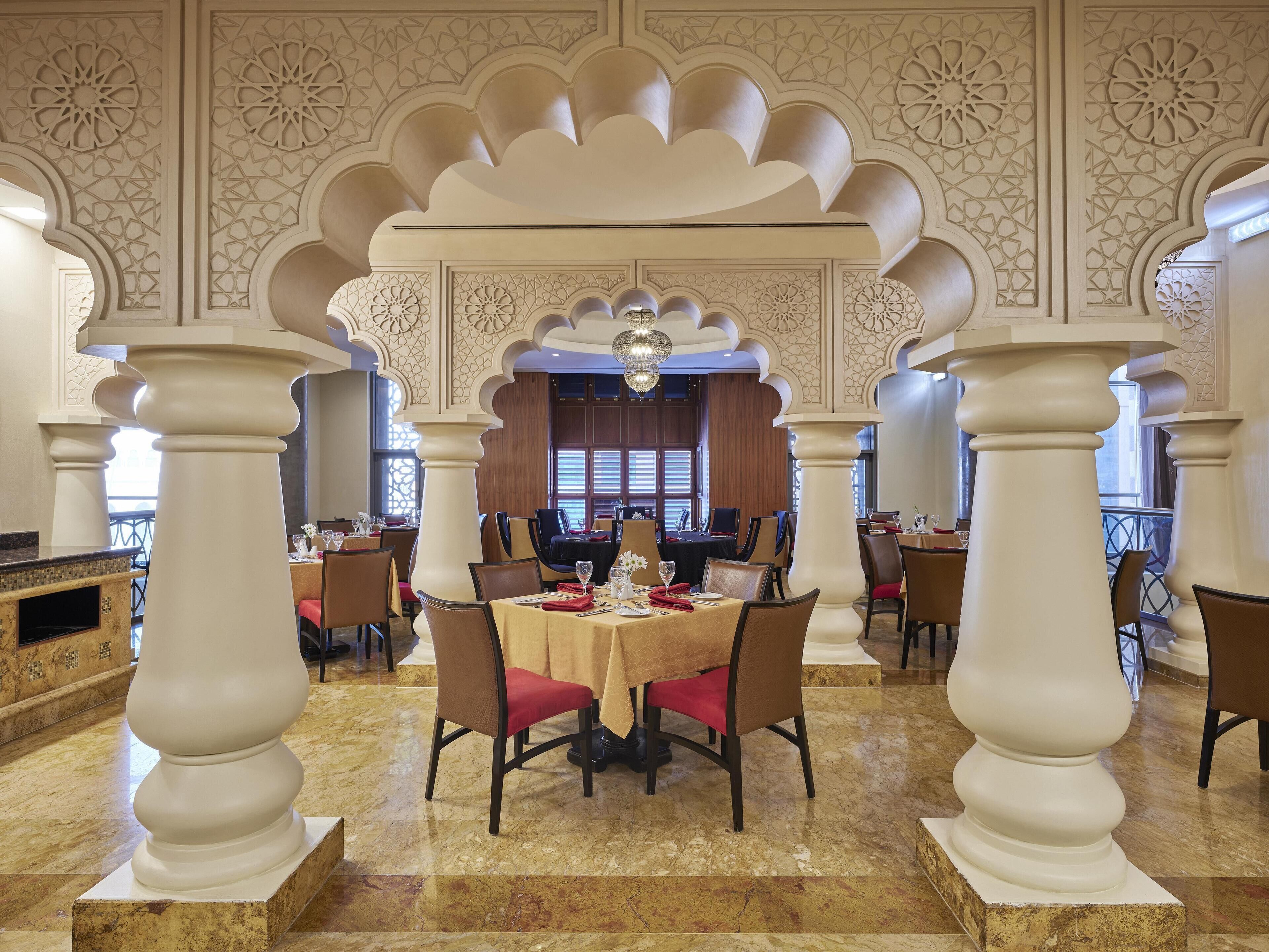 A dining area with marble floors, tables set with red napkins, and white pillars with intricate carvings.