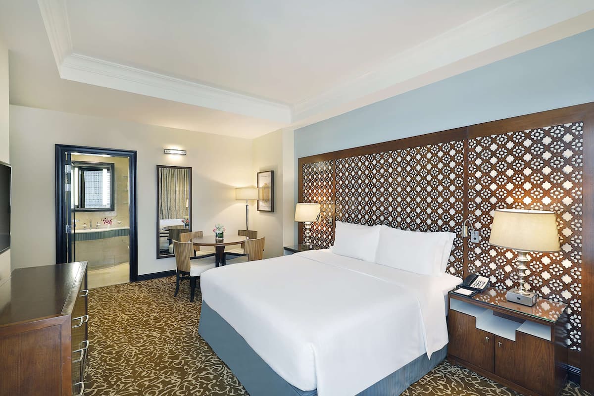 Habitación de hotel con una cama grande, un escritorio con silla, una mesita y una mesita de noche con lámpara.