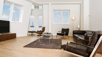 A modern living room with a flat-screen TV, leather sofas, and a large window offering a view of the city skyline.