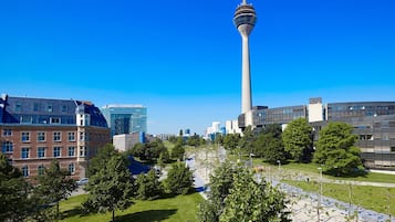 A modern cityscape with a prominent tower, a mix of modern and traditional architecture, and a well-maintained public park area.