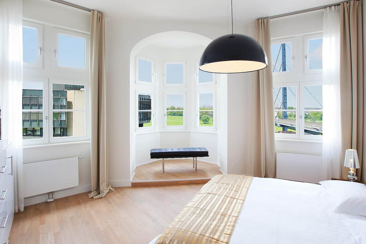 Une chambre d’hôtel moderne avec un grand lit, un banc et une vue sur un pont et la verdure.