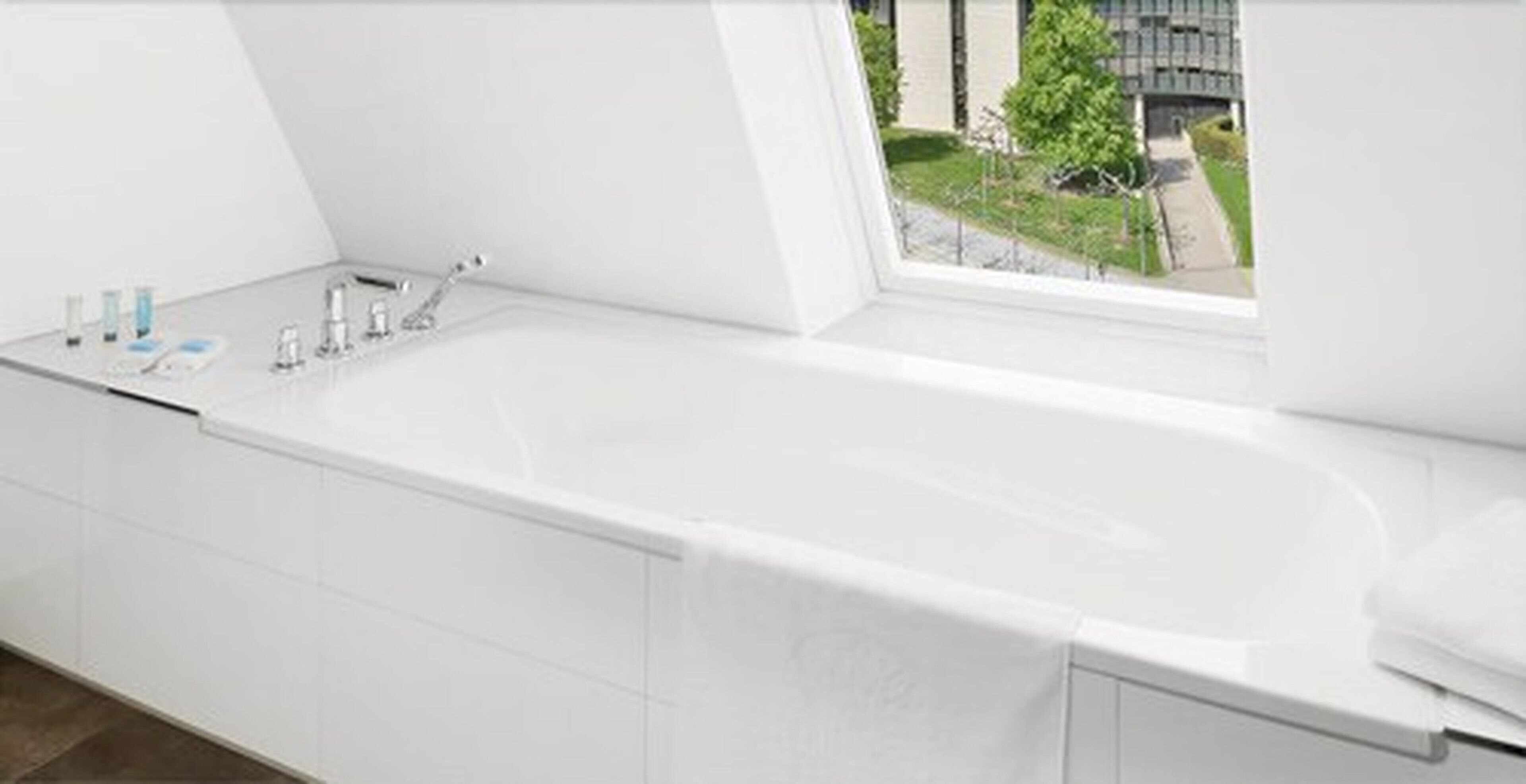 Un baño moderno con una bañera grande, una ventana con vista a un edificio y follaje exterior.