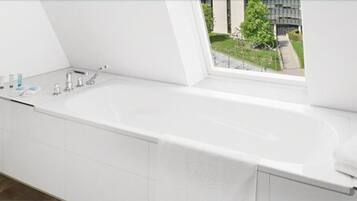 Un baño moderno con una bañera grande, una ventana con vista a un edificio y follaje exterior.