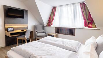 Ein Hotelzimmer mit Bett, Schreibtisch mit Computer, Stuhl, Wandfernseher und einem fensterbepflanzten Fenster.