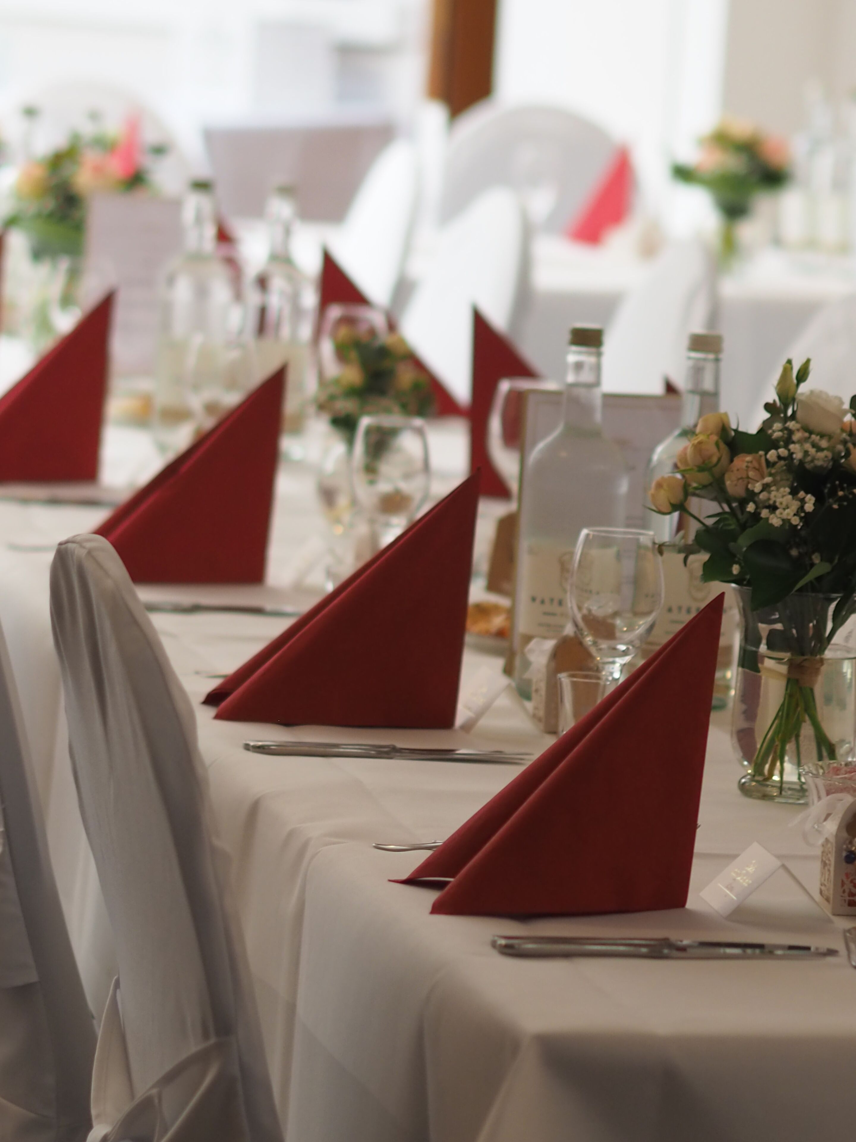 A table set with red napkins, clear glassware, and a vase with flowers.