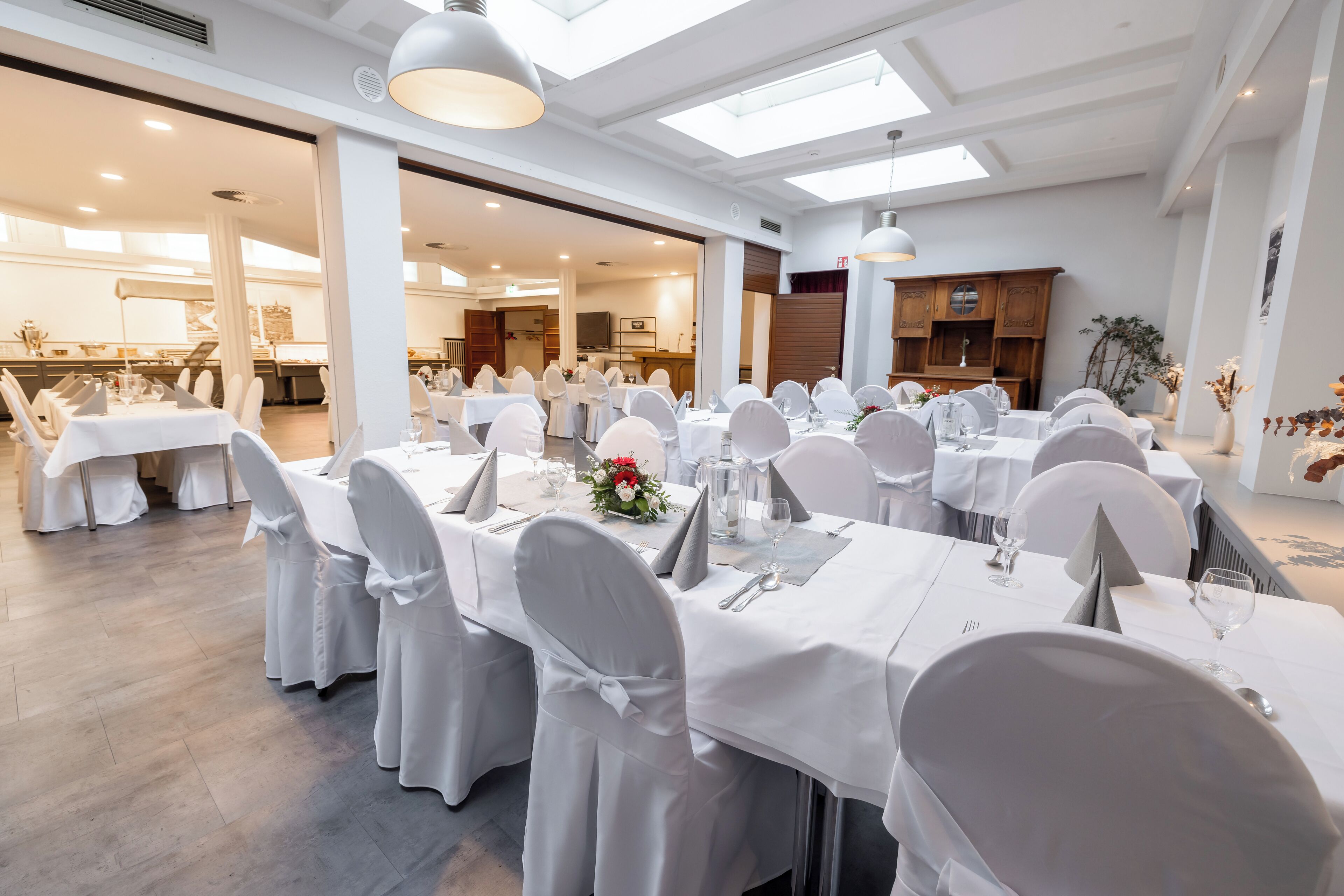 A banquet hall with multiple tables set for a formal event, featuring white tablecloths and chairs, and a modern interior design.