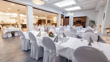 A banquet hall with multiple tables set for a formal event, featuring white tablecloths and chairs, and a modern interior design.